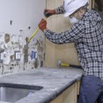 Pracownik remontowy usuwający płytki ścienne w kuchni podczas remontu domu.