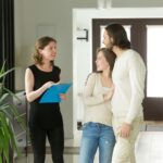 Przyjazny pośrednik w obrocie nieruchomościami lub wynajmujący, pokazujący nowoczesny luksusowy dom na sprzedaż młodej parze klientów, agent nieruchomości omawiający wynajmowany dom z najemcami, planujący koncepcję zakupu nieruchomości